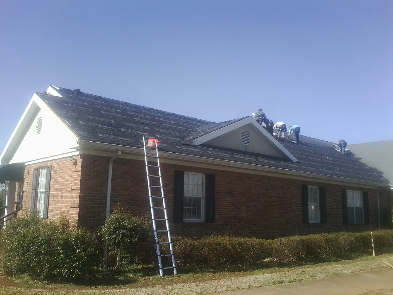 Crew tearing shingles off a brick ranch roof with a ladder set — Metal Roof Repair work by our crew in Jacksonville