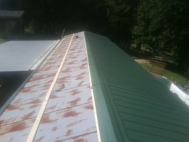 Old rusted panels beside newly installed green metal roofing — Wind Damage Roof Repair by Roofing Brothers in Jacksonville